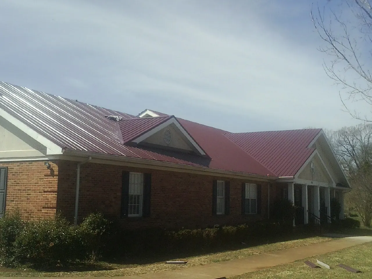 Red metal roof with gabled entries on a long brick building, from a Hail Damage Roof Repair job in Rutland
