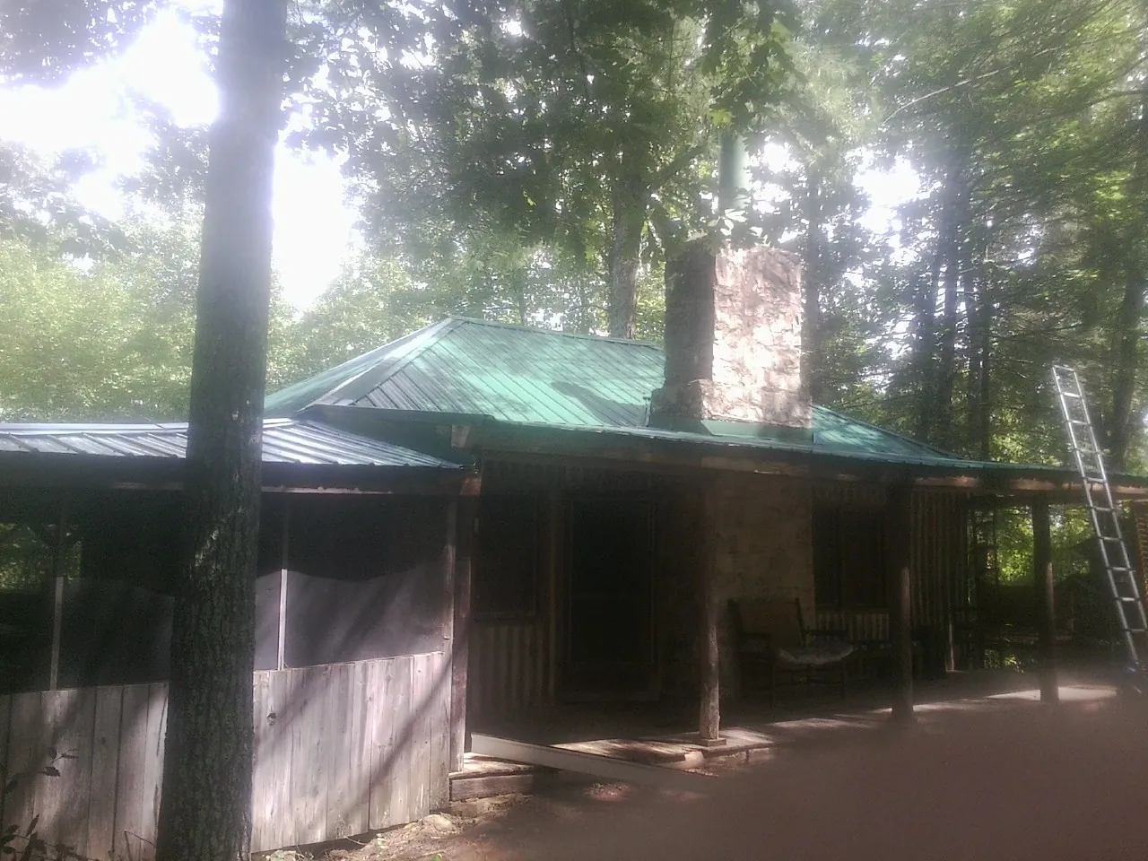Green metal roof and stone chimney above a log cabin porch in Rutland